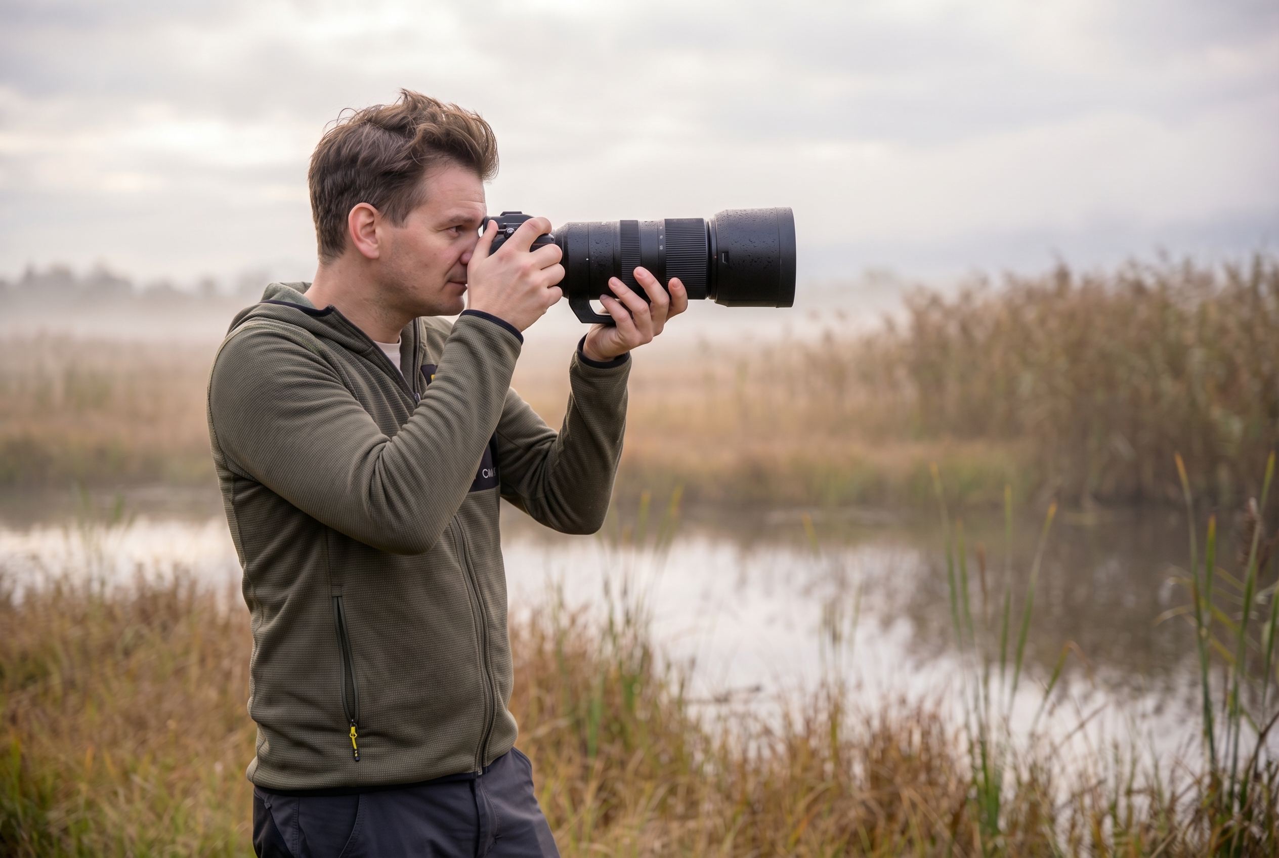 Photographe animalier en extérieur tenant un téléobjectif professionnel à l'aube, illustrant le matériel nécessaire pour débuter la photo animalière.
