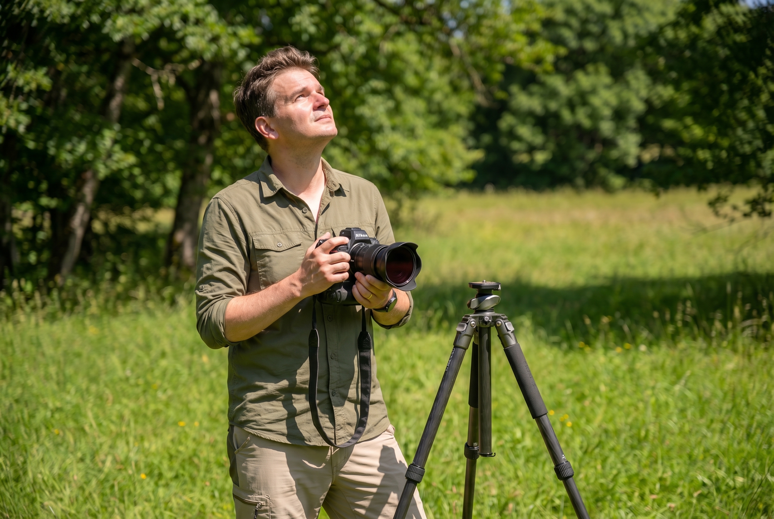 Photographe naturaliste tenant un appareil photo hybride avec un filtre infrarouge vissant, préparant ses réglages dans une prairie en plein soleil.