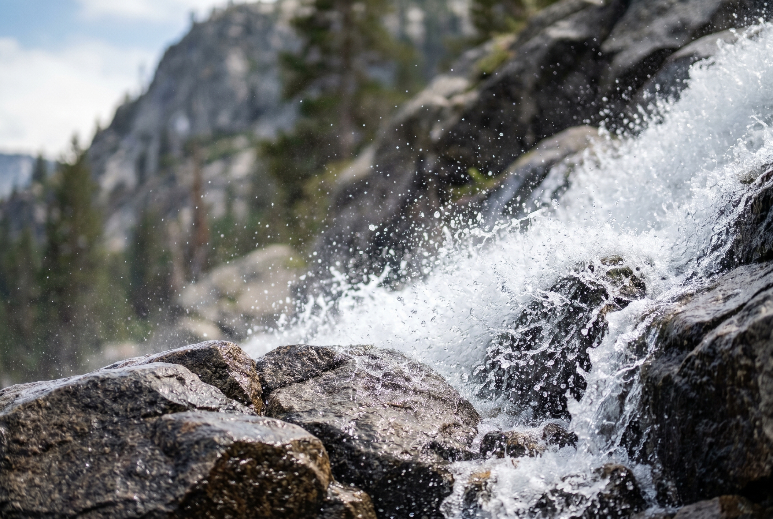 Photographie d'une cascade de montagne avec gouttelettes d'eau figées par une vitesse d'obturation rapide sur des rochers de granit sombre.