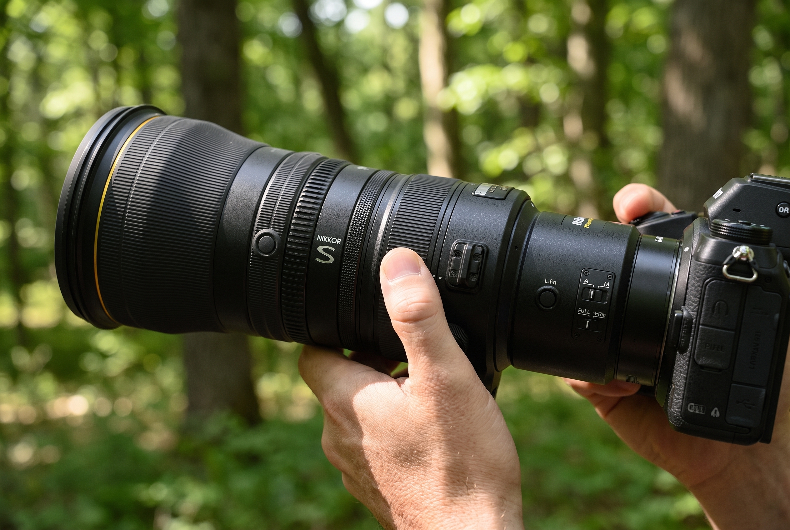 Gros plan sur la main d'un photographe actionnant le commutateur du téléconvertisseur intégré de l'objectif Nikon Z 600mm f/4 TC VR S en forêt.